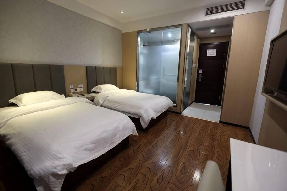 A hotel room with two beds, a bathroom with a glass door, and a TV.