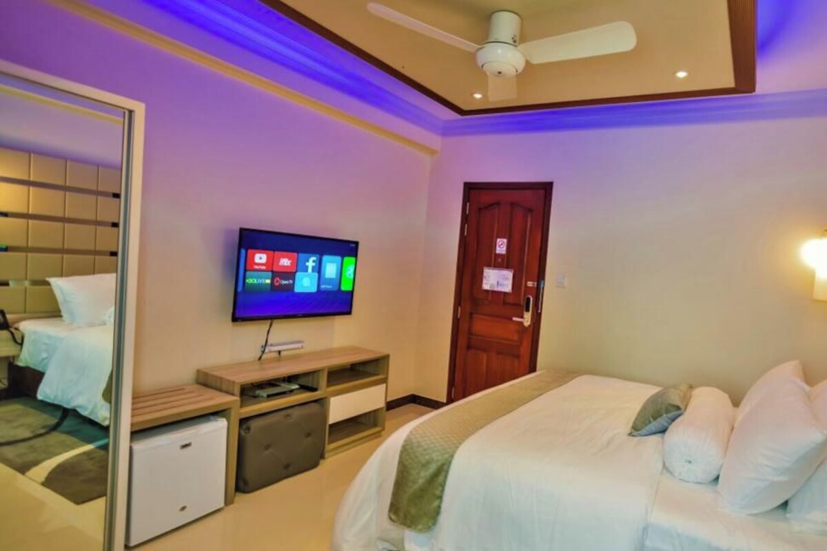 A hotel room with a bed, a television mounted on the wall, a small desk, and a wardrobe.