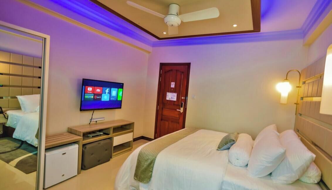 Ein Schlafzimmer mit einem Bett, einem Fernseher, einem Deckenventilator, einer Tür und einer wandmontierten Leuchte.