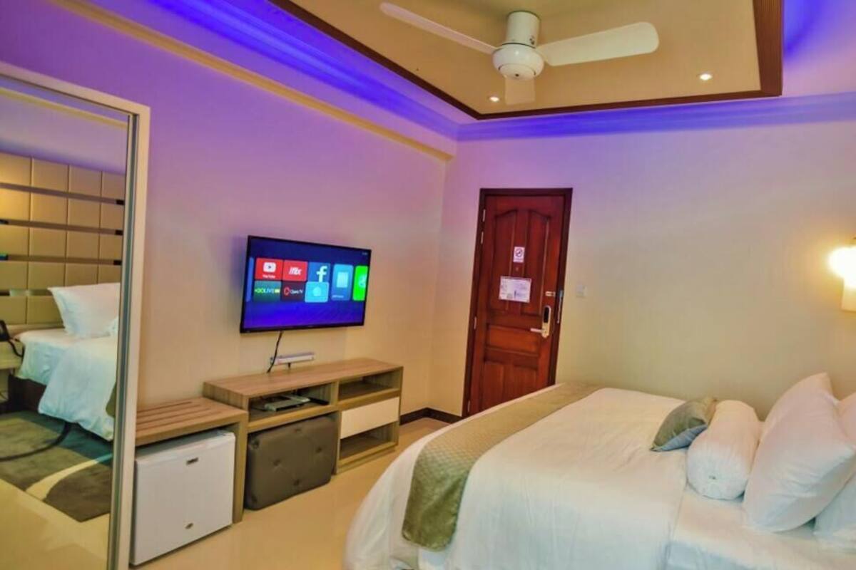 A bedroom with a bed, a television, a ceiling fan, a door, and a wall-mounted light fixture.