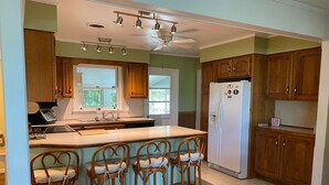 A kitchen with wooden cabinets, a white refrigerator, a built-in oven, a microwave, a sink, and a bar stool area. - Topridge - Spacious 3BR home w/fenced yard, pet friendly NO LINENS PROVIDED (Chincoteague)