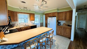 A kitchen with wooden cabinets, a large island with bar stools, a refrigerator, and a ceiling fan. - Topridge - Spacious 3BR home w/fenced yard, pet friendly NO LINENS PROVIDED (Chincoteague)