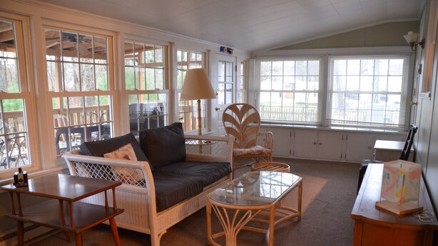 A cozy living room with a sofa, a glass coffee table, wicker chairs, and large windows. - Topridge - Spacious 3BR home w/fenced yard, pet friendly NO LINENS PROVIDED (Chincoteague)