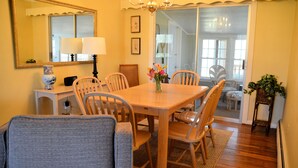A dining area with a wooden table, six chairs, a vase with flowers, a lamp, and a mirror on the wall. - Topridge - Spacious 3BR home w/fenced yard, pet friendly NO LINENS PROVIDED (Chincoteague)