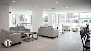 Un amplio y moderno salón con diversas opciones de asientos, incluyendo sofás y sillones, grandes ventanales que aportan luz natural y un diseño limpio y minimalista.