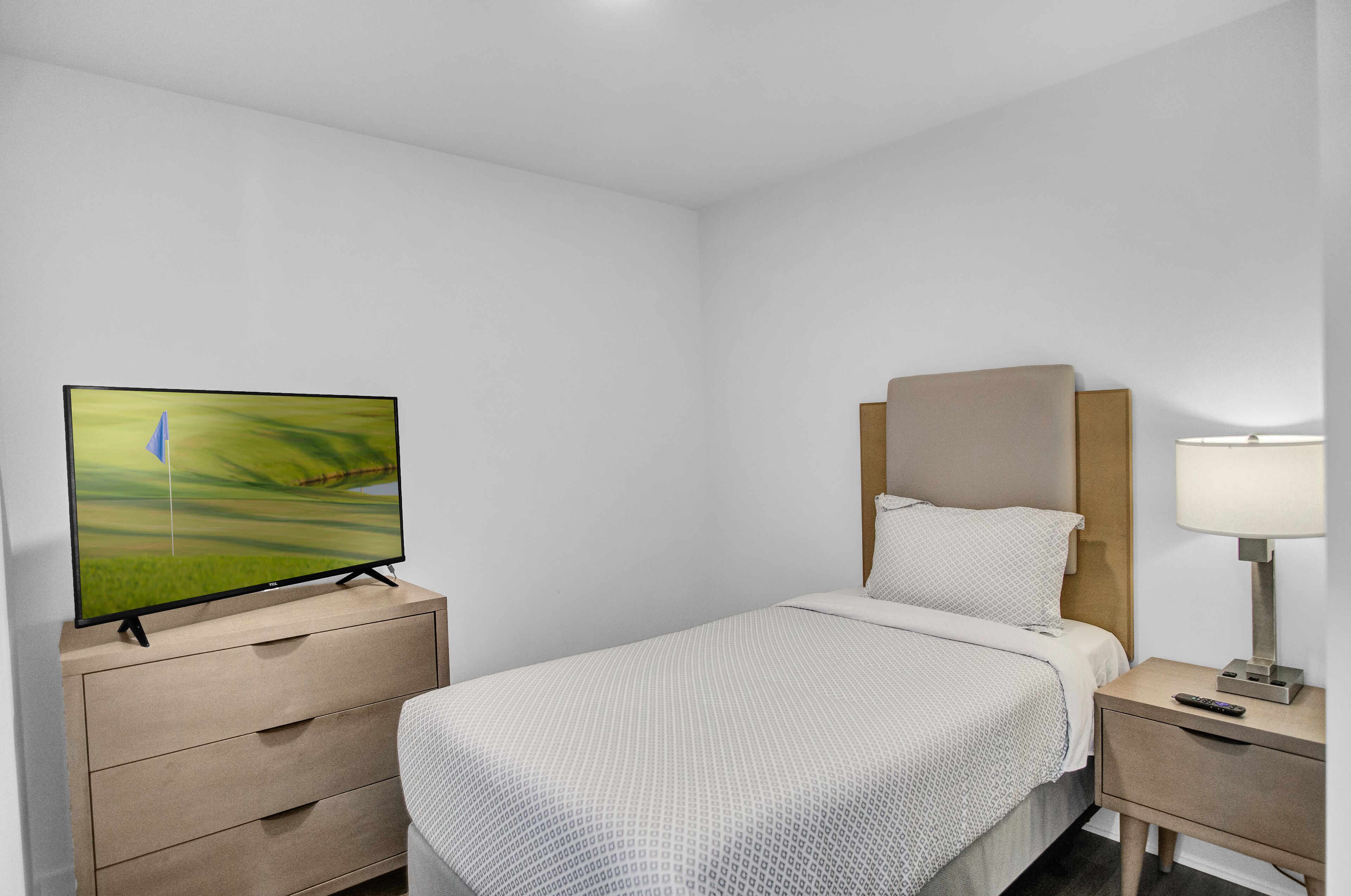 Ein Hotelzimmer mit einem Bett, einem Fernseher auf einem Schrank, einem Nachttisch mit Lampe und einem Holzkopfteil.