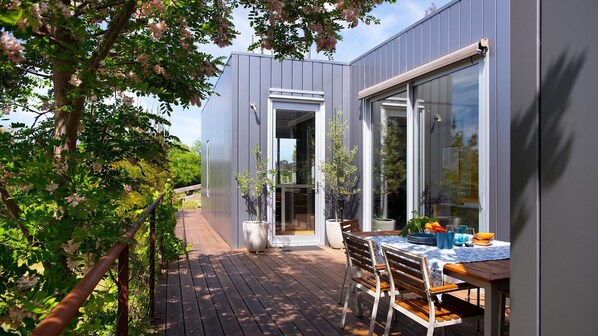 A modern outdoor patio with a wooden deck, a table with chairs, and potted plants.