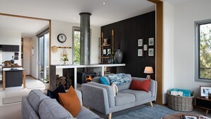 A modern living room with a grey sofa, a fireplace, and a dining area visible through an open door. - Kirkwood - Pet Friendly - Mid Century - Walking distance to Clunes! (Clunes)