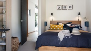 A modern bedroom with a large bed, a wooden headboard, and two wall-mounted lamps. - Kirkwood - Pet Friendly - Mid Century - Walking distance to Clunes! (Clunes)