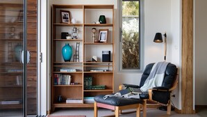 A cozy reading nook with a leather chair, a bookshelf filled with books, a lantern, and a view of the outdoors through a window. - Kirkwood - Pet Friendly - Mid Century - Walking distance to Clunes! (Clunes)