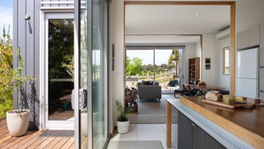 A modern kitchen with a wooden countertop, a dining area with a table and chairs, and a view of the outdoors through large sliding glass doors. - Kirkwood - Pet Friendly - Mid Century - Walking distance to Clunes! (Clunes)