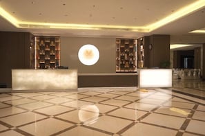 Un hall d’hôtel comprenant un comptoir d’accueil, un luminaire circulaire et un sol carrelé.