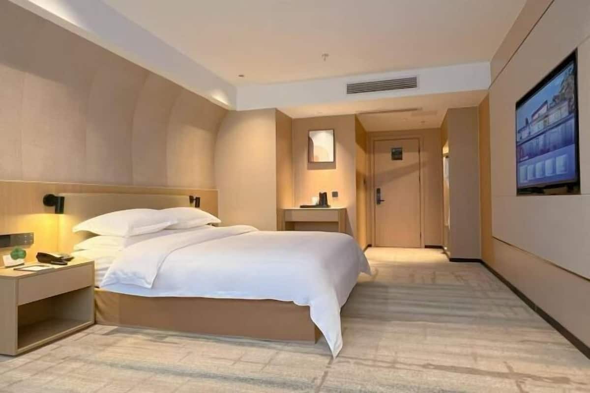 A hotel room with a bed, bedside table, lamp, and a TV on the wall.