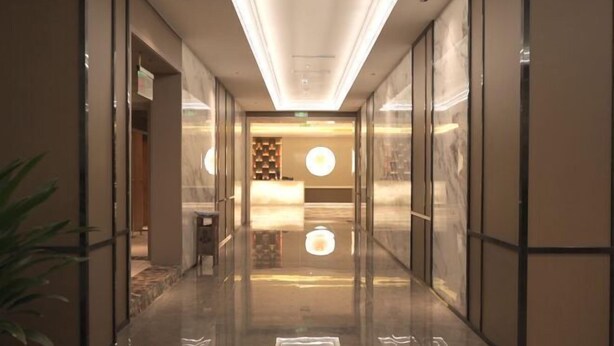 Un hall d’hôtel moderne doté d’un sol réfléchissant, de cloisons en verre et d’un espace de réception agrémenté d’un luminaire circulaire.
