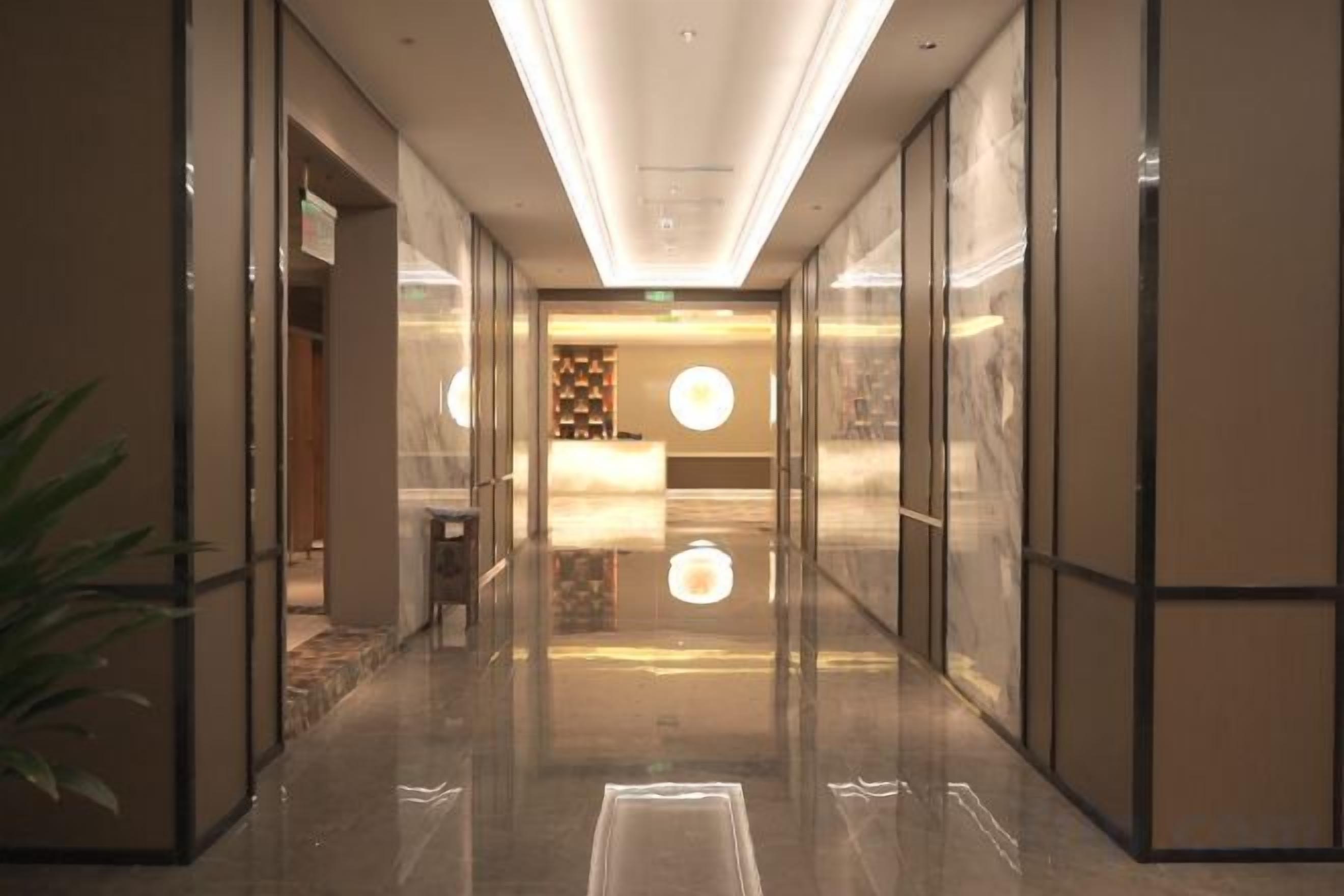 A hotel lobby with a reception desk, a plant, and a reflective floor.