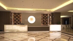 Un hall d’hôtel comprenant un comptoir d’enregistrement, un bureau de réception et un grand luminaire circulaire fixé au mur.
