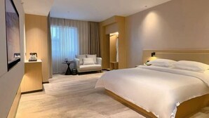 Une chambre d’hôtel avec un grand lit, une chaise, une petite table et une fenêtre avec des rideaux.
