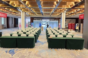 Un salón de conferencias con filas de mesas y sillas, una alfombra estampada y un diseño de techo moderno.