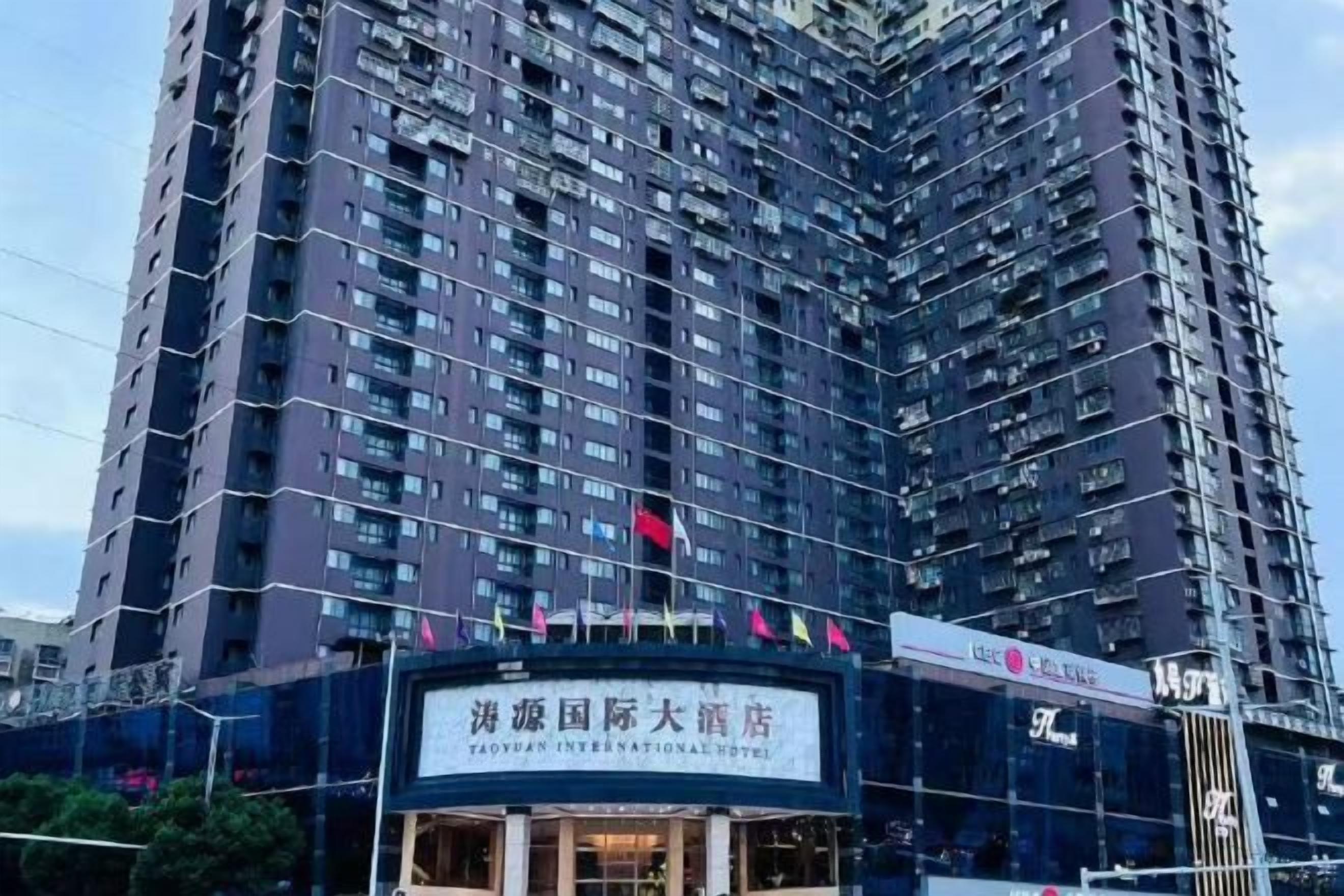 Un edificio de gran altura con varios pisos, un cartel que indica que es el Hotel Internacional Taoyuan, y una bandera en la cima.
