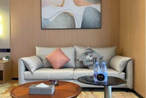 A modern hotel room with a leather sofa, a round coffee table with a tissue box and water bottles, and a large abstract painting on the wall. - Taoyuan International Hotel (Dazhou)