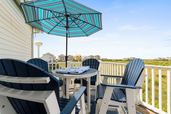 A deck with Adirondack chairs, a striped umbrella, and a table with a towel.
