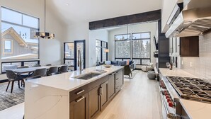 Une cuisine moderne dotée d’un grand îlot central, d’appareils électroménagers intégrés et de grandes fenêtres.
