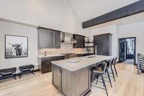 Et moderne køkken med en stor ø, mørke træskabe og et højt loft med synlige bjælker.