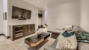 Un salon moderne doté d’un téléviseur à écran plat, d’un meuble de rangement en bois foncé, d’une table basse noire et d’un canapé gris agrémenté de coussins à motifs.