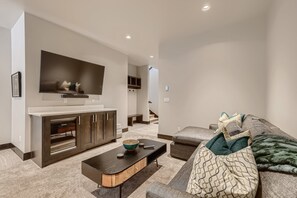A modern living room with a flat-screen TV, dark wood entertainment unit, a black coffee table, and a grey sofa with patterned cushions.