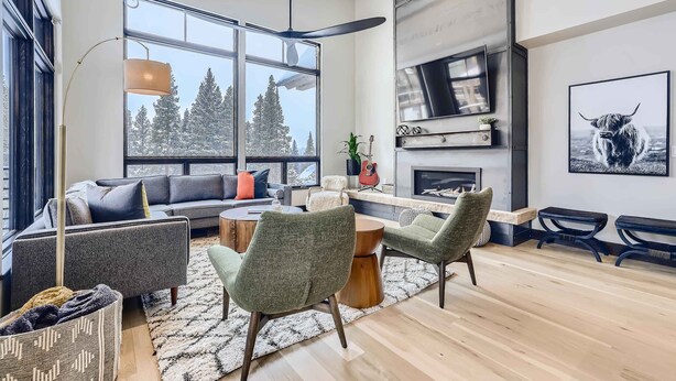 Un salon moderne avec un canapé, des fauteuils, une cheminée et une grande fenêtre donnant sur la forêt.