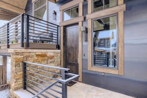 A modern building with a stone base, a metal balcony railing, and a large window.