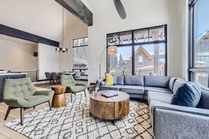 A modern living room with a sectional sofa, armchairs, a coffee table, and large windows offering a view of a snowy landscape.
