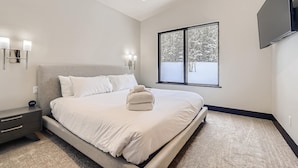 Une chambre moderne avec un grand lit, des lampes de chevet, un téléviseur à écran plat et une fenêtre donnant sur la forêt.