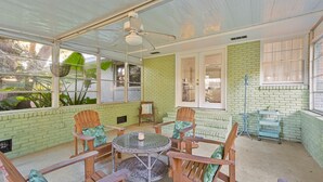 A covered patio with a glass table, wooden chairs, and a ceiling fan. - Artist's Cottage - Comfortable Pet friendly home 1 mile from the beach! (St Simons Island)