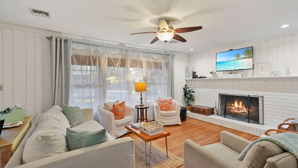 A living room with a fireplace, white walls, and a ceiling fan. - Artist's Cottage - Comfortable Pet friendly home 1 mile from the beach! (St Simons Island)