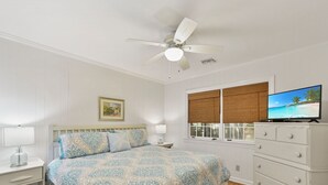 A bedroom with a bed, nightstands, a dresser, a ceiling fan, a window with blinds, and a television. - Artist's Cottage - Comfortable Pet friendly home 1 mile from the beach! (St Simons Island)