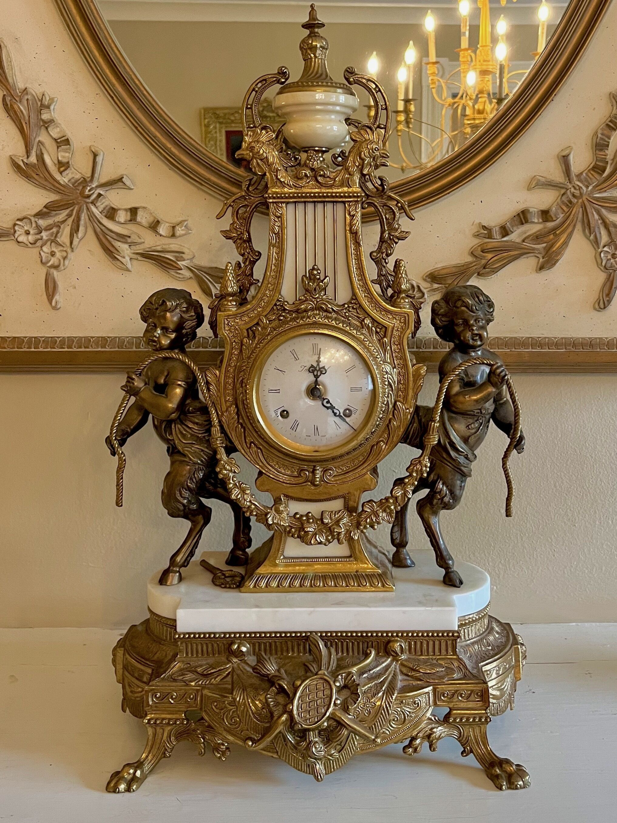 Un reloj de pie ornamentado con dos querubines, frente a una pared con molduras decorativas y un espejo.