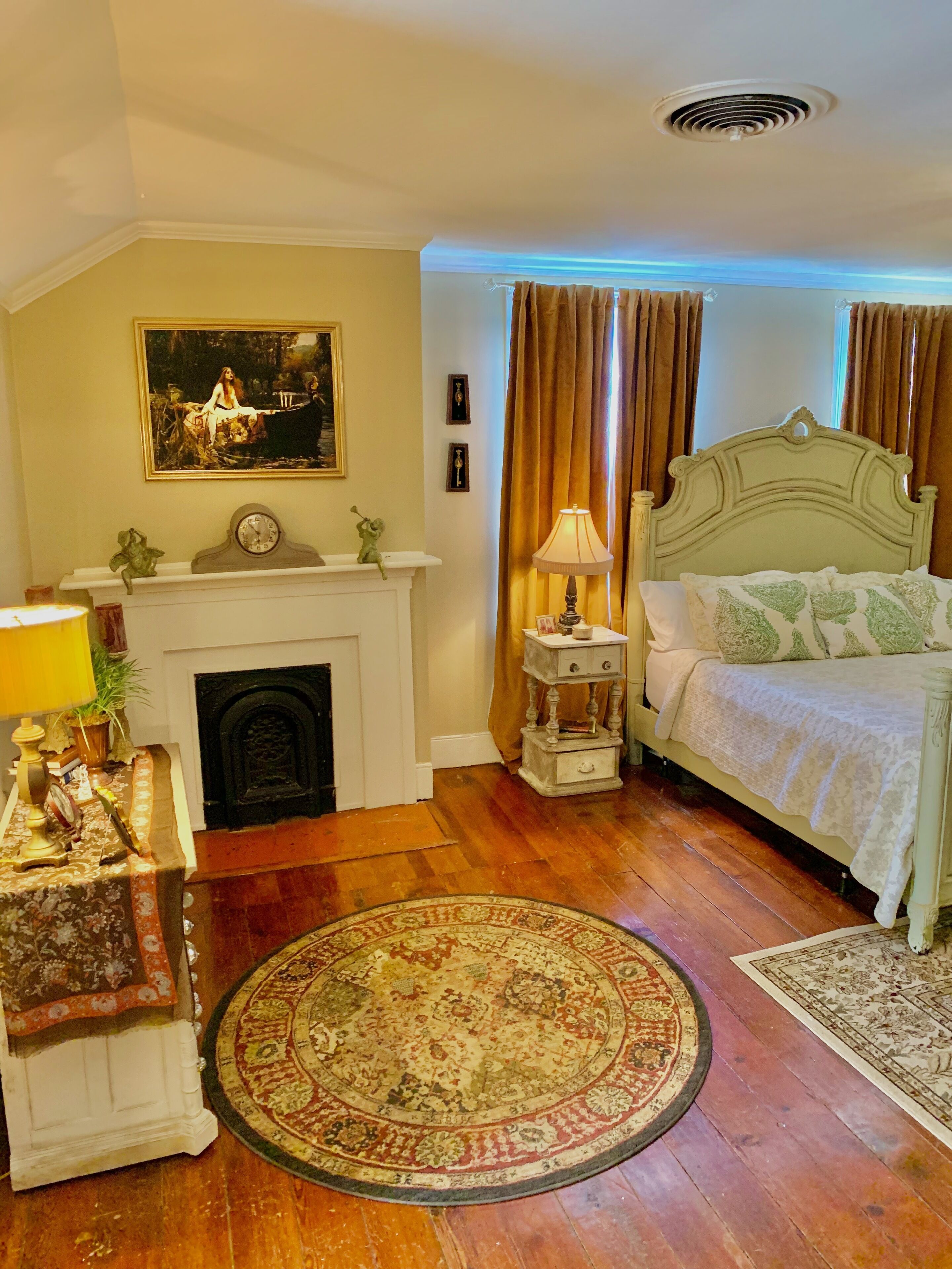A bedroom with a bed, a fireplace, a nightstand, a lamp, and a rug.