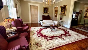 A spacious living room with a large, ornate chandelier, a patterned area rug, and classic furniture including a sofa and armchairs. - The Beaumont House (Natchez)