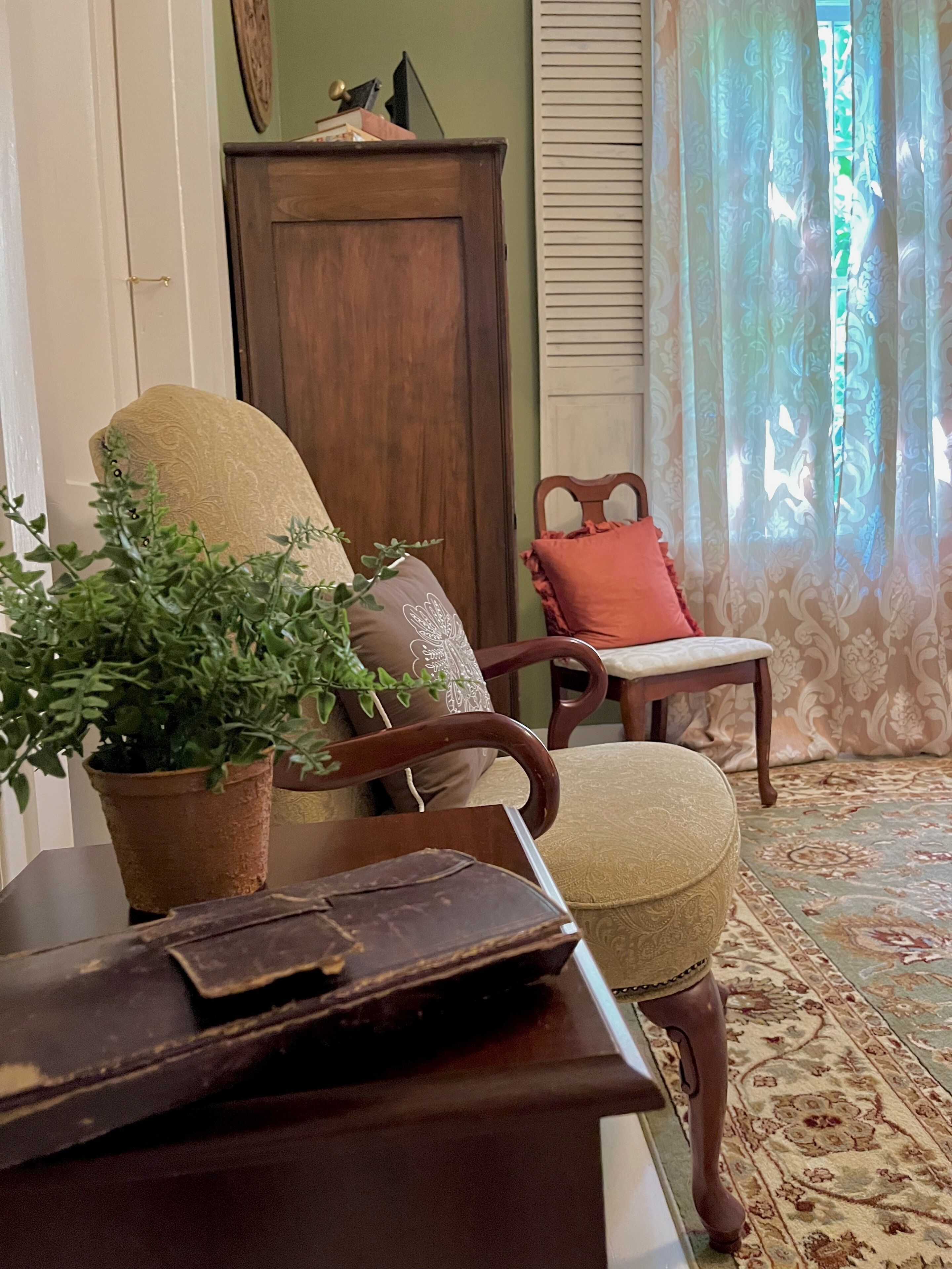 A room with a wooden chair, a small table with a plant and a book, and a cabinet against the wall.