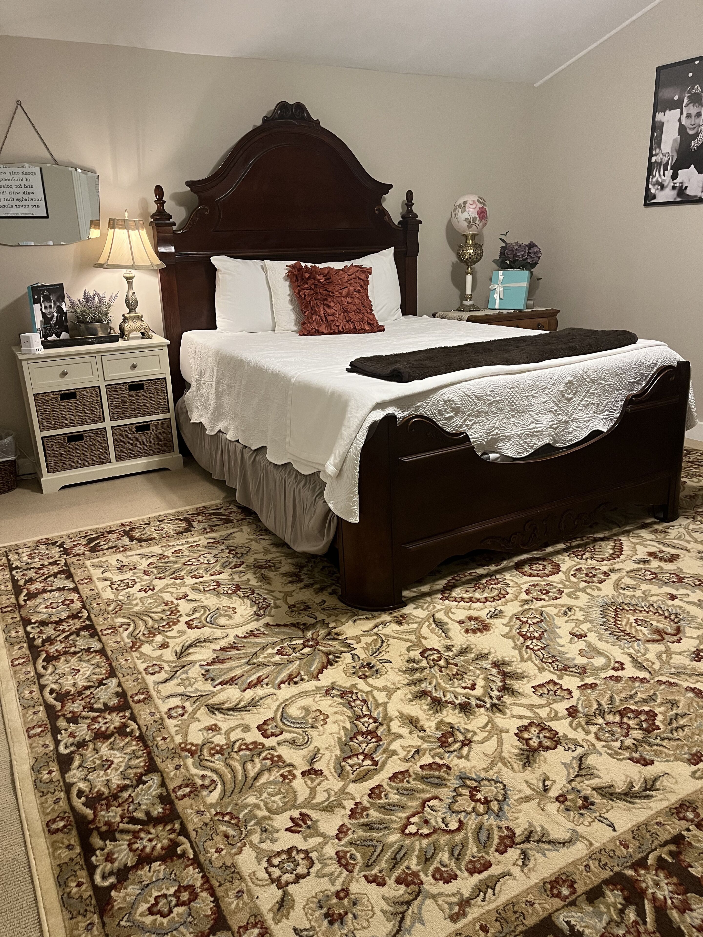 Un dormitorio con una cama grande, una mesita de noche, una lámpara, un aparador y una alfombra estampada.