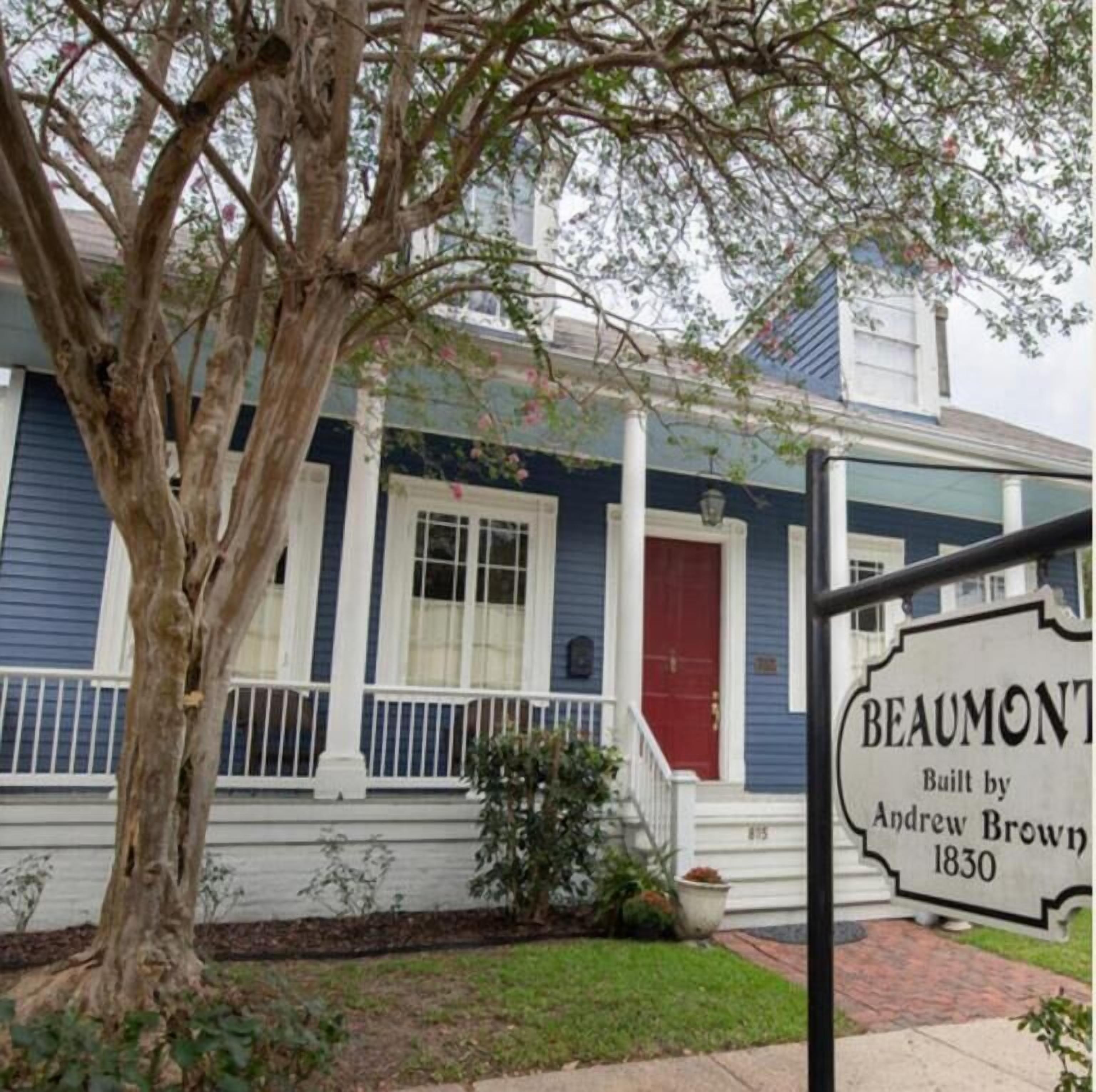 A historic house with a blue exterior, white trim, and a red door. A sign indicates it was built by Andrew Brown in 1830.