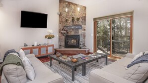 A living room with a stone fireplace, a flat-screen TV, and a large sliding glass door to the outdoors. - Vail Point #7 4 Bedroom Townhouse by RedAwning (Vail)