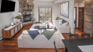 A modern living room with a fireplace, a flat-screen TV, a dining area, and a sliding glass door to the patio. - Vail Point #7 4 Bedroom Townhouse by RedAwning (Vail)