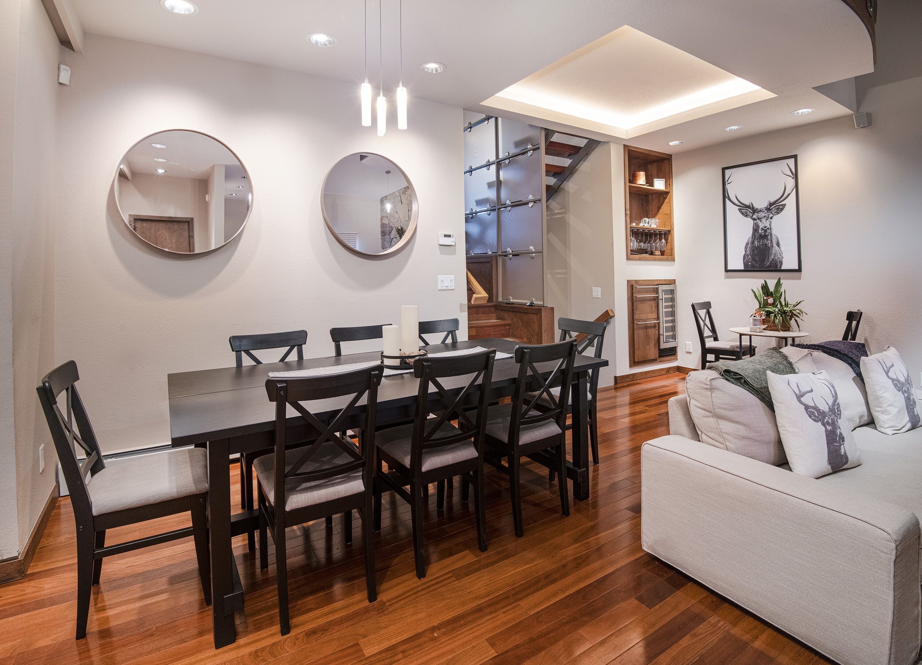 A modern dining area with a wooden table and chairs, a sofa, and a staircase leading to an upper level.