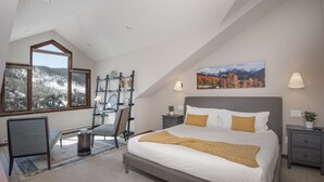 A bedroom with a large bed, a desk, and a chair. There are windows with a view of trees and mountains. - Vail Point #7 4 Bedroom Townhouse by RedAwning (Vail)