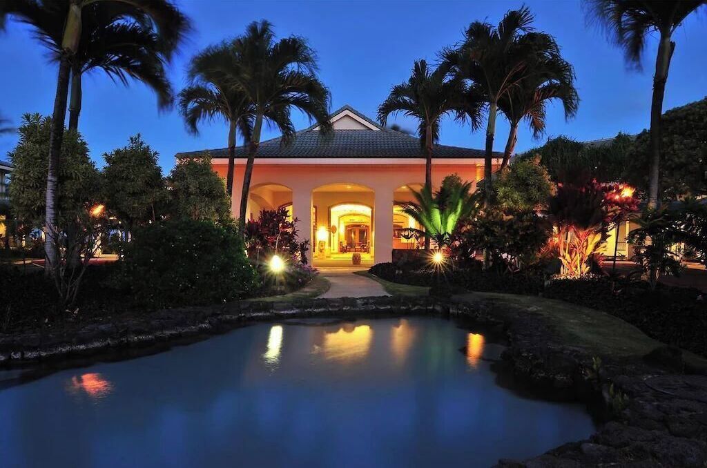 A resort with a pool, palm trees, and a well-lit entrance.