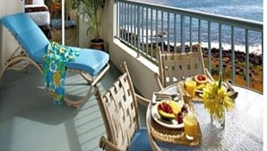 Un balcó amb vistes a l'oceà, una taula de dinar amb fruita i suc, i una cadira de relaxació.