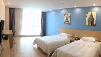 A hotel room with two beds, a desk, a chair, and a window with curtains.