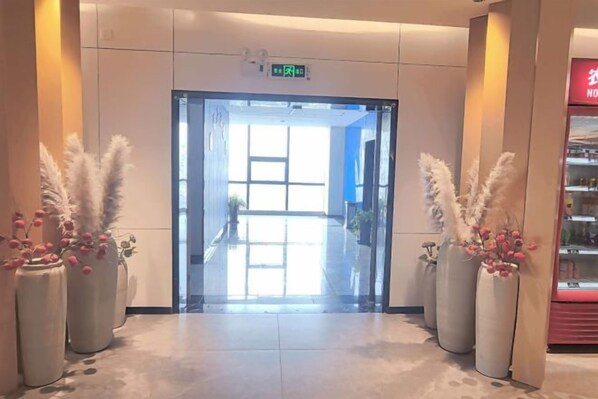 Un vestíbulo de hotel con puerta de vidrio, plantas en macetas y un expendedor.